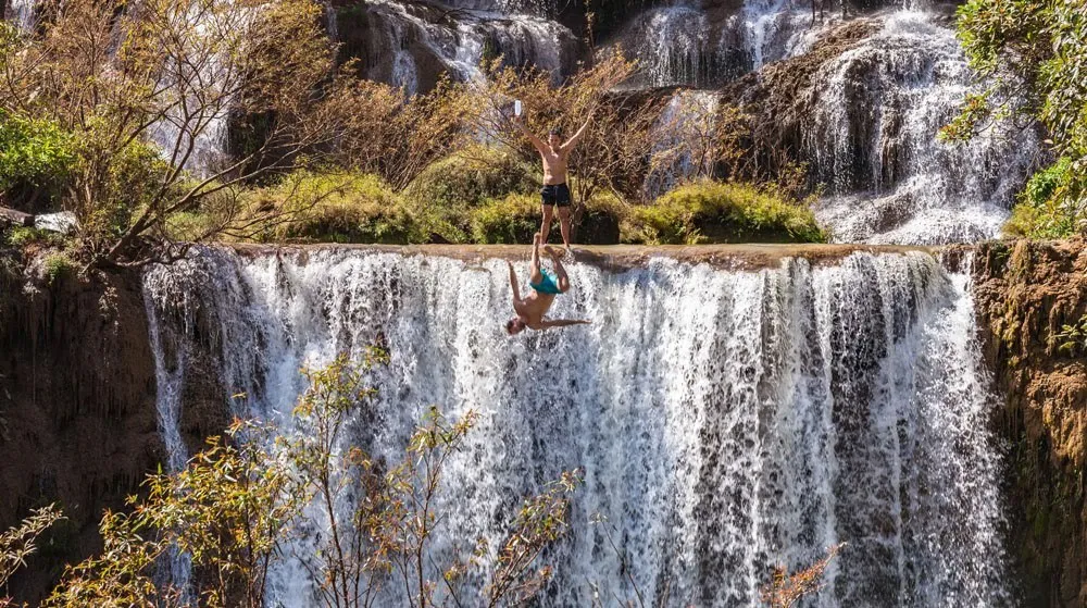 Thi Lor Su waterfall thundering over jungle cliffs, tiny figures below.