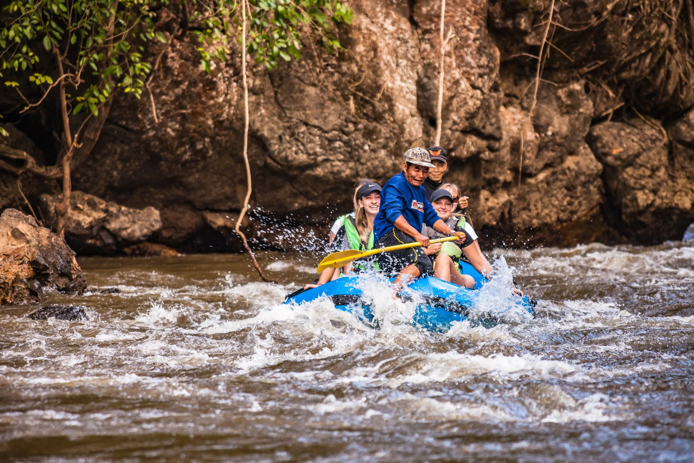 A raft full of travellers paddling through whitewater rapids on a jungle river.