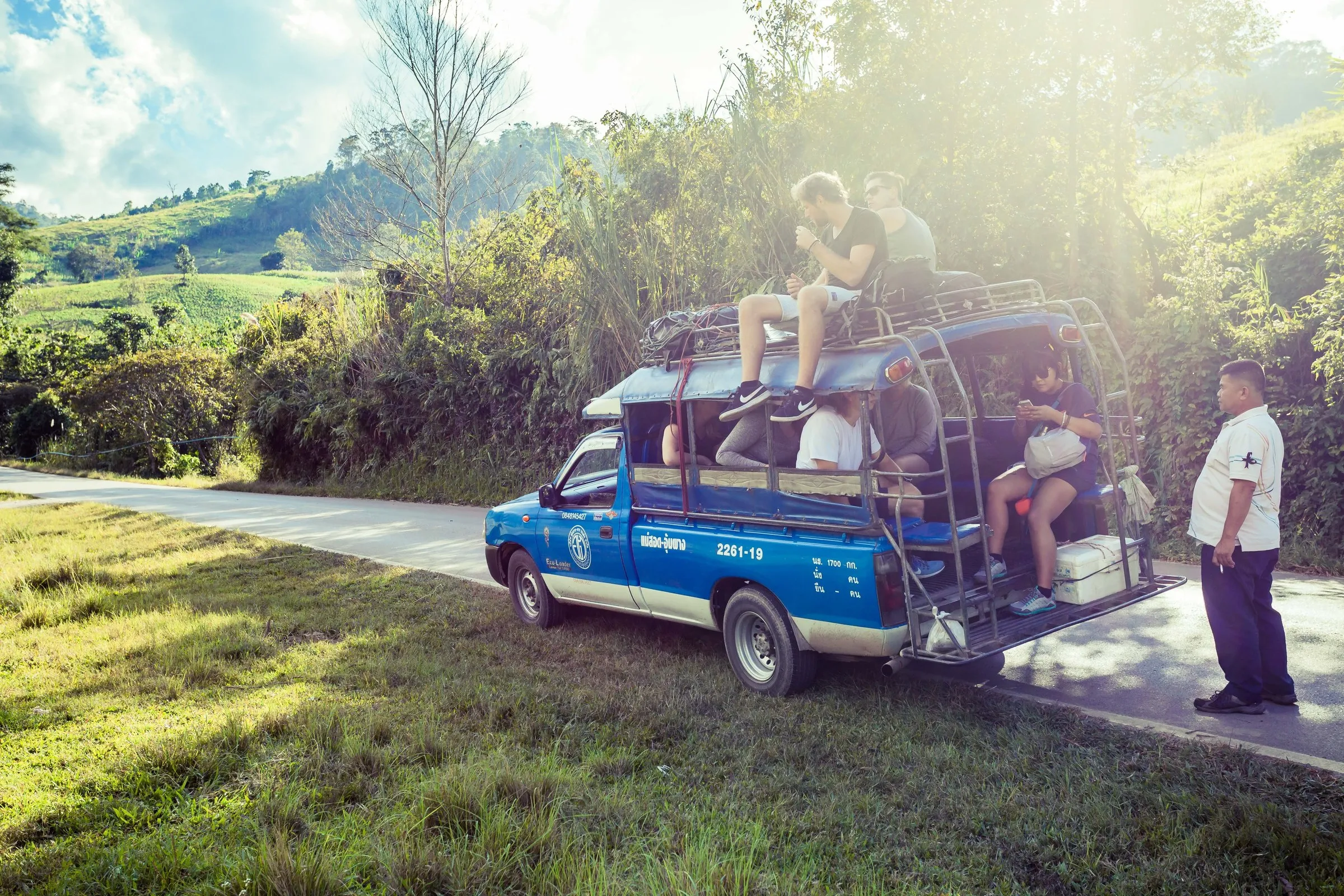 A blue songthaew truck stopped on the winding mountain road to Umphang, travellers riding on the roof.
