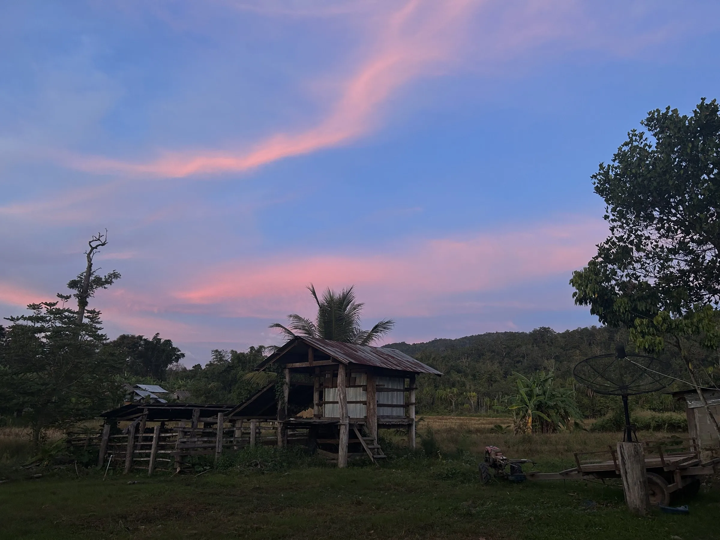 A wooden Karen village house in Palatha under a pastel dusk sky.