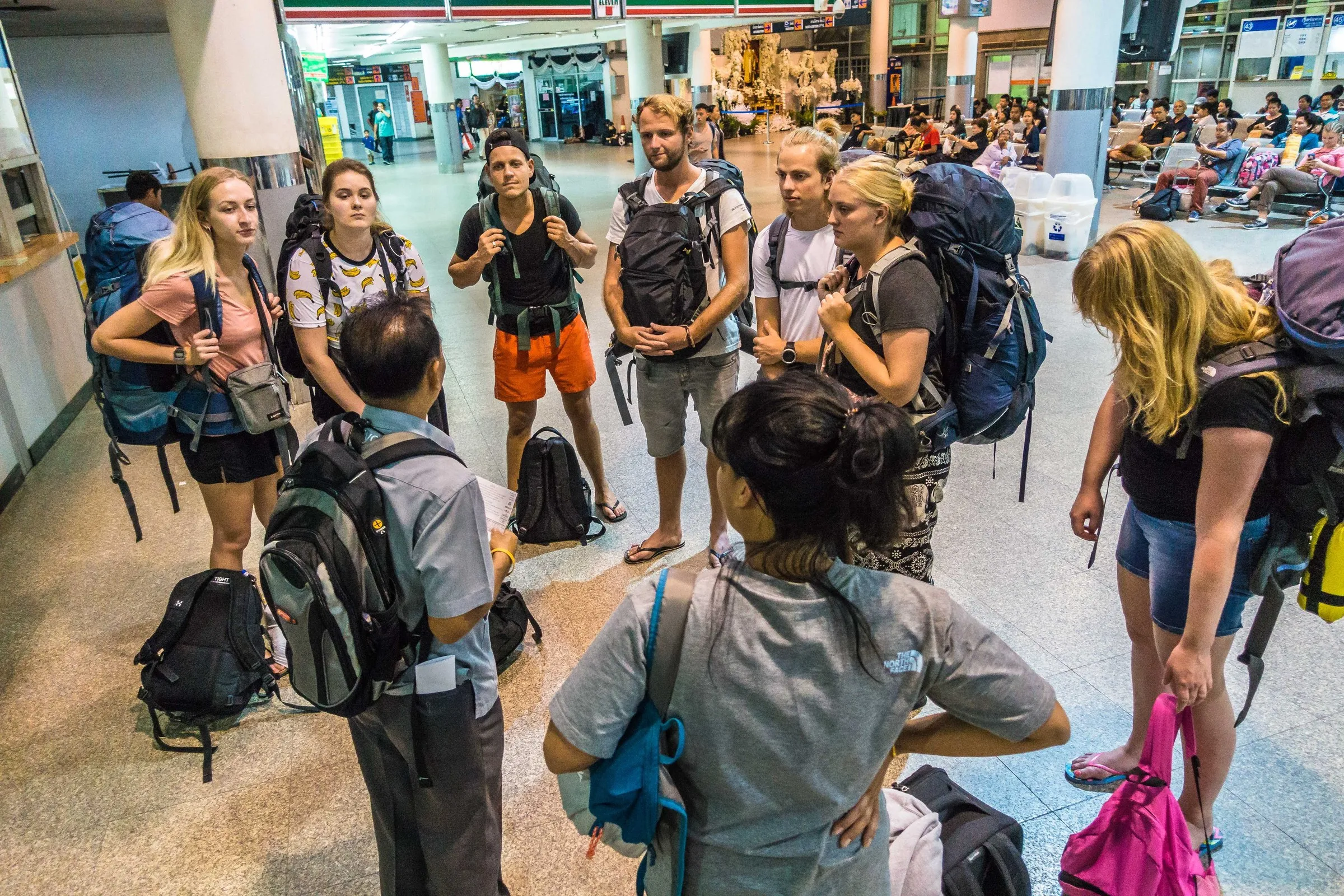 Travellers with their backpacks gathered around the guide at Bangkok’s Mo Chit bus station.