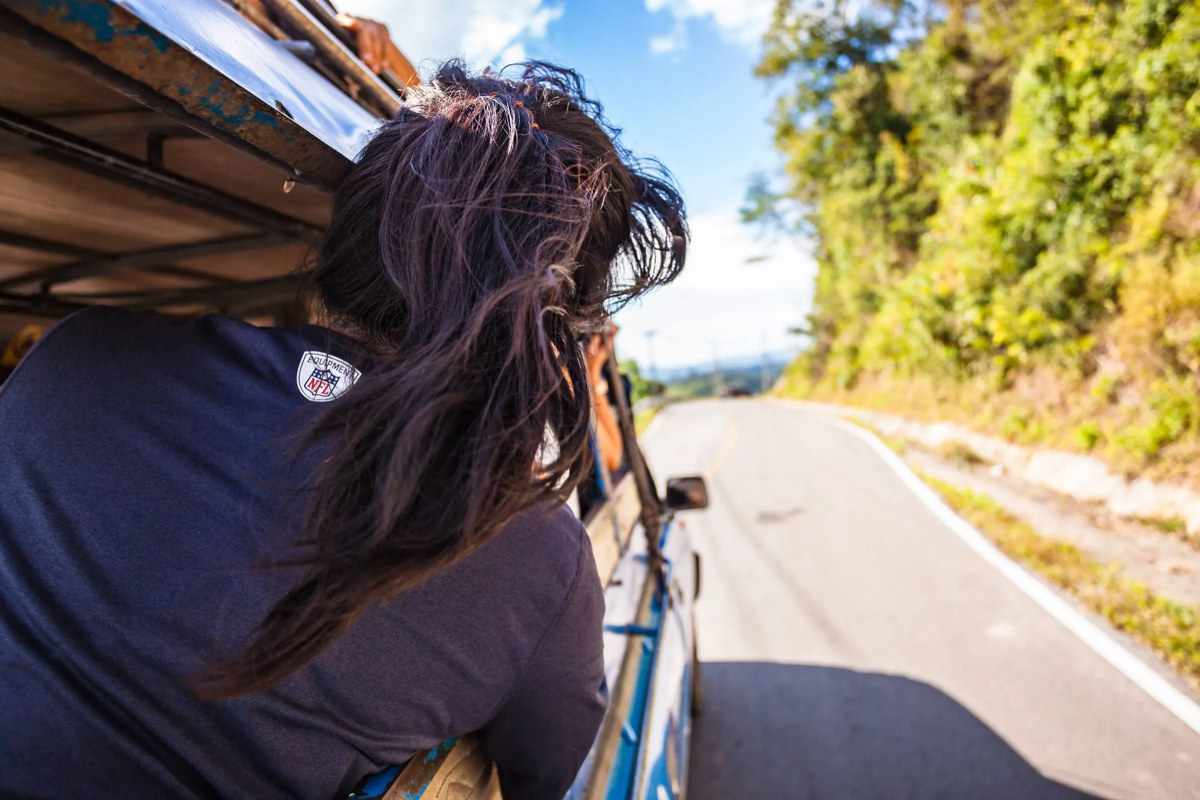 View from the roof of a songthaew rolling down an empty road between forested hills.