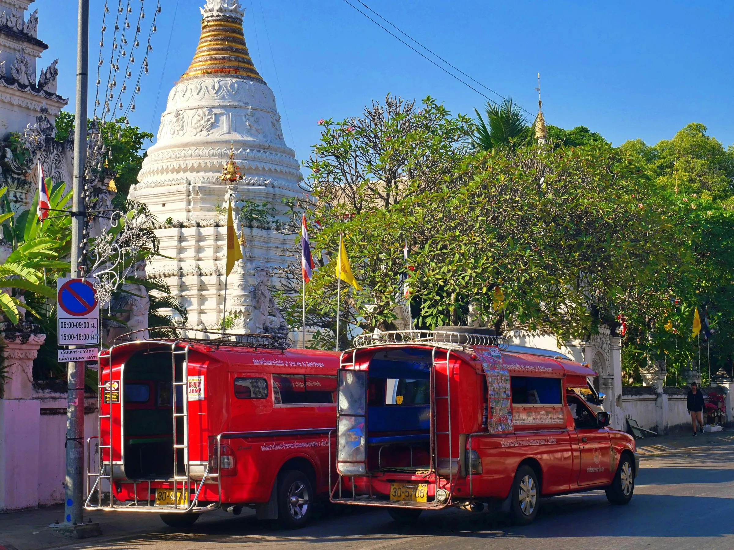 Two red songthaews parked in front of a white-and-gold temple in Chiang Mai.